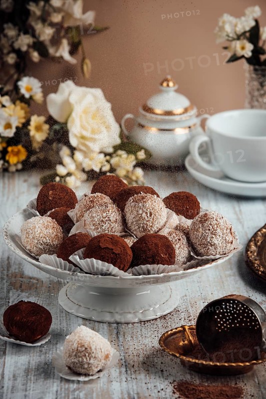 Elegantly arranged tiramisu, chocolates on a porcelain plate next to flowers and a cup