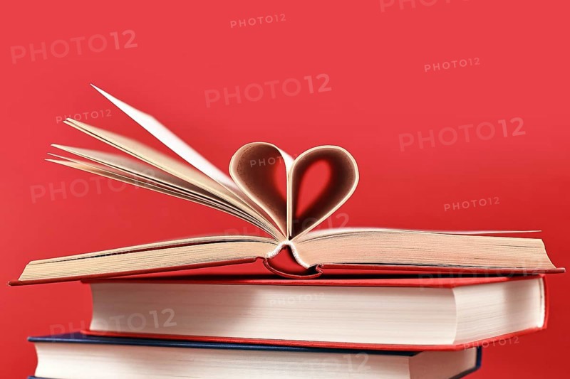 Pages folded into heart shape on stack of old hardcover books on red background