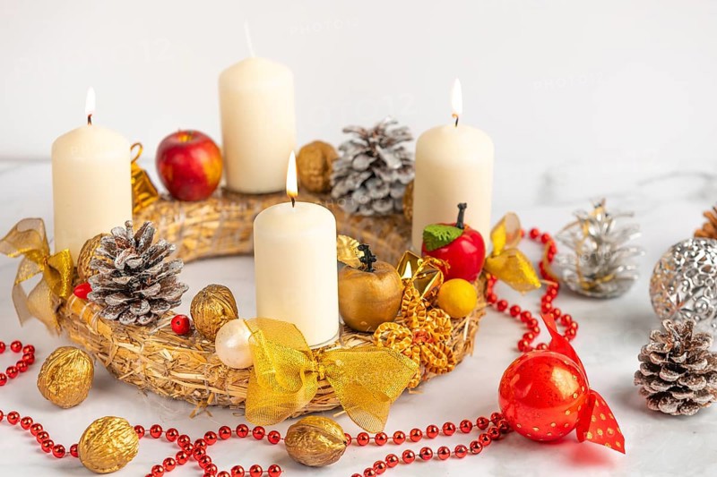 Advent wreath with three burning candles, red pearl necklace and Christmas decorations next to it