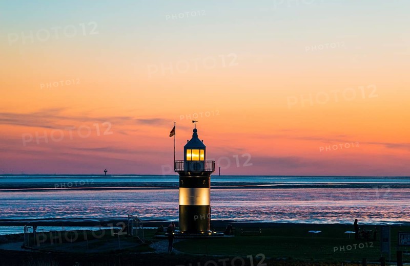 Black and white lighthouse, called 'Kleiner Preuße', lighthouse and boat at sunset on the coast, sky in warm colours, sky changes from blue to orange, the sea calm and peaceful, shortly after sunset, twilight, evening, dusk, Sea in the background, coast, meadow and lamp in the foreground, calm atmosphere, maritime, North Sea resort Wremen, Lower Saxony Wadden Sea National Park, World Heritage Site, Wurster North Sea coast, Land Wursten, district of Cuxhaven, Lower Saxony, Germany, Europe
