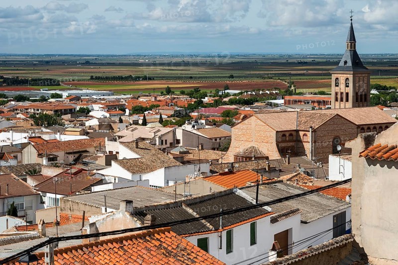 A town view with red roofs and a church tower in the distance under a cloudy sky, Campo de Criptana, Ciudad Real province, Castilla-La Mancha, Route of Don Quixote, Spain, Europe