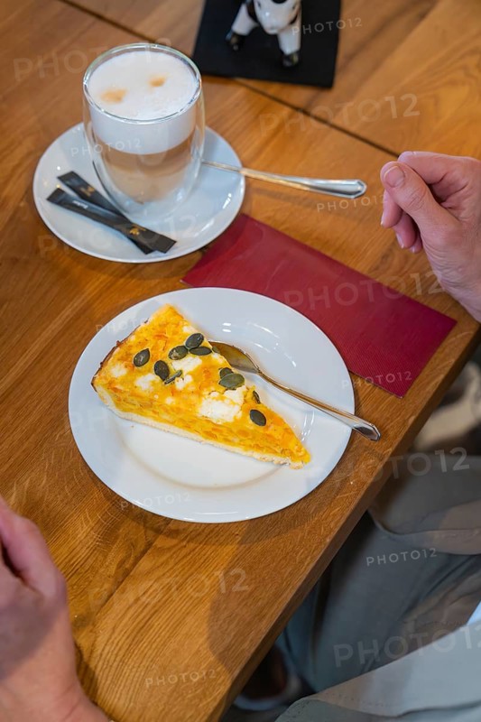 A slice of pumpkin pie on a plate and a cup of latte macchiato on a wooden table, autumn creations at Cafe Kuh, Deckenpfronn, Germany, Europe