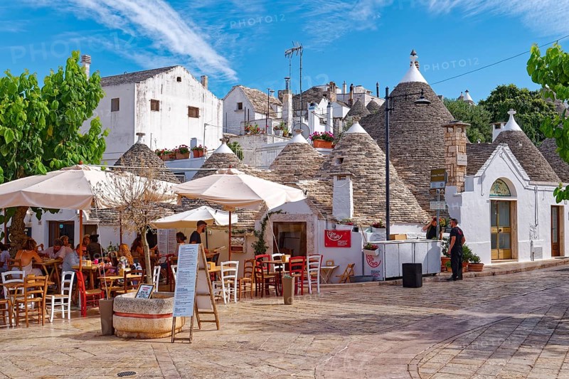 Whitewashed trulli, round houses with stone roofs, in the southern Italian town of Alberobello. In the foreground, a restaurant on Via Monte Santo. The historic town centre, which is entirely built up with trulli, is a UNESCO World Heritage Site. Alberobello, Apulia, Southern Italy, Southern Europe