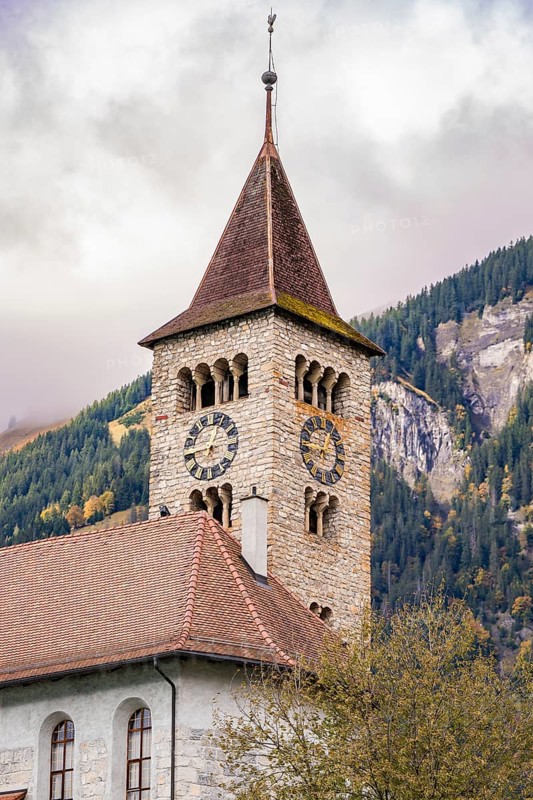 A traditional stone church tower in front of an autumnal wooded mountain, Lake Brienz, Switzerland, Europe