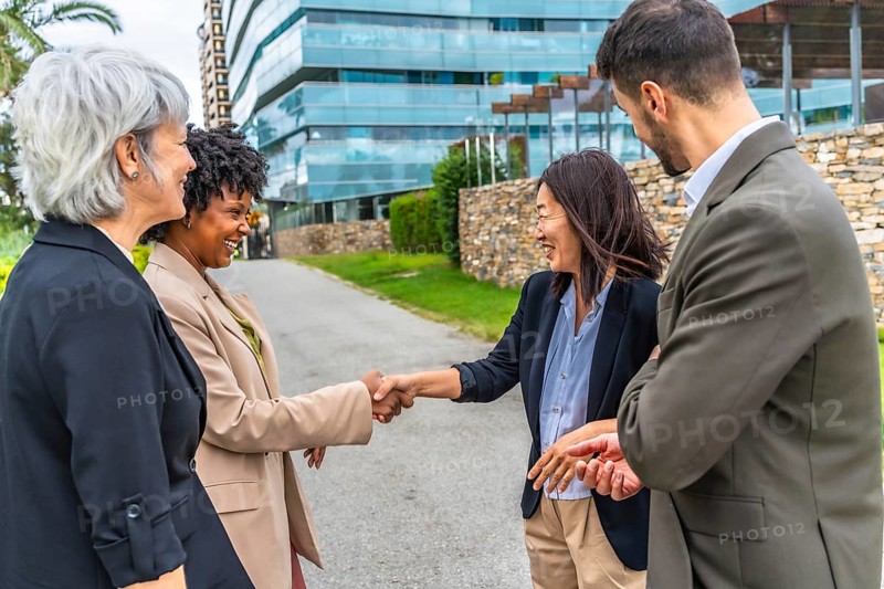 Multi-ethnic businesswomen shaking hands during outdoor meeting next to business colleagues in the city