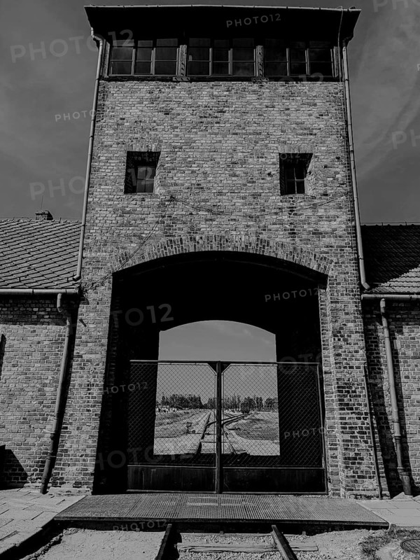 A historic brick building with a watchtower and gate, featuring rail tracks in front. Auschwitz-Birkenau, Poland, Europe