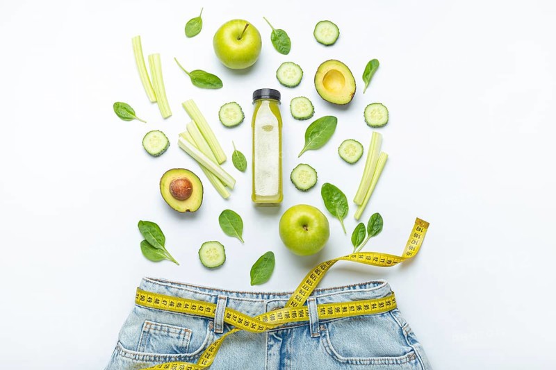 Green fruit, vegetables, smoothie falling into jeans and yellow measuring tape instead of belt on white background. Concept of healthy food for weight loss, detox, diet, healthy clean nutrition, food photography, food photography