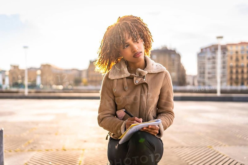 Pensive beauty latin woman writing notes sitting on the city with urban landscape on the background on a cold day
