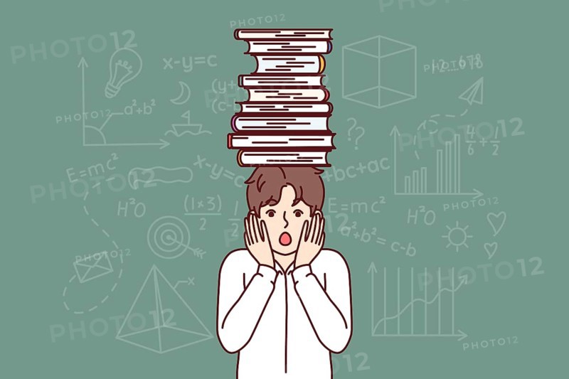 Frightened schoolboy with books on head feels fear of exam, stands near blackboard with formulas. Schoolboy experiences stress due to complex educational program for primary school students