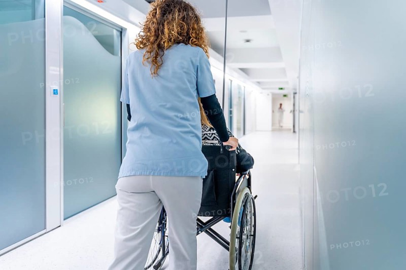 Rear view of a nurse pushing wheelchair with woman along the corridor of an hospital