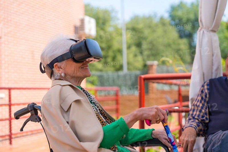 An elderly woman with the nurse looking through virtual reality glasses in the garden of a nursing home, vr glasses