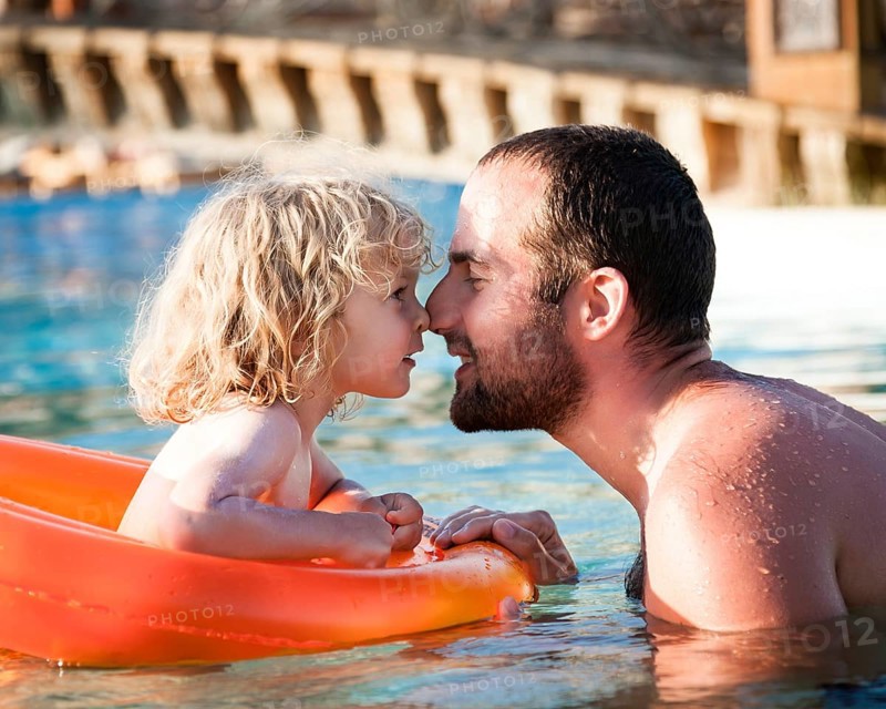 Happy child playing with father in blue water of swimming pool on a tropical resort at the sea. Summer vacations concept