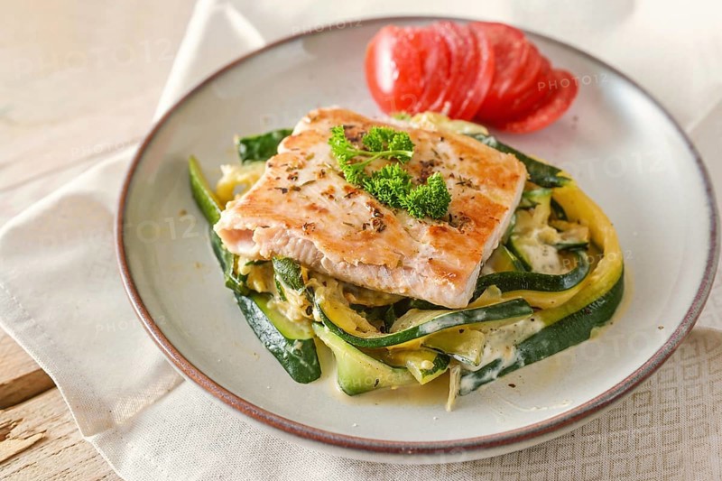 Fried wild salmon with parsley garnish on zucchini vegetables and fresh tomato on a light plate, healthy meal for a low carb diet, selected focus, narrow depth of field