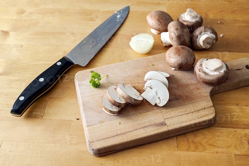 Mushrooms whole and sliced on a wooden cutting board and a kitchen knife, preparation for cooking a healthy vegetarian meal, copy space, selected focus, narrow depth of field