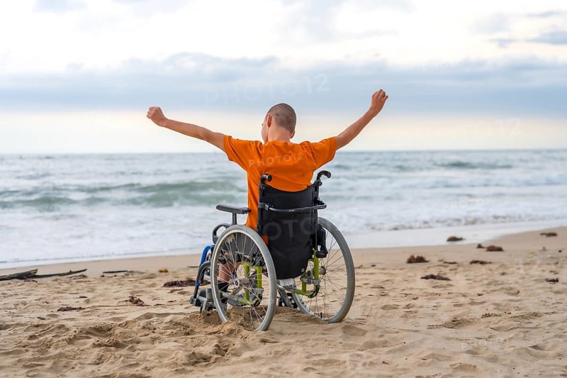 Disabled person on his back in a wheelchair on the beach with open arms enjoying the freedom