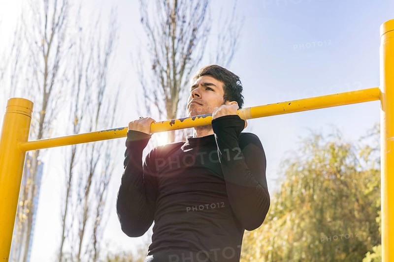 Attractive man doing pull-ups exercises on a crossbar in a public park