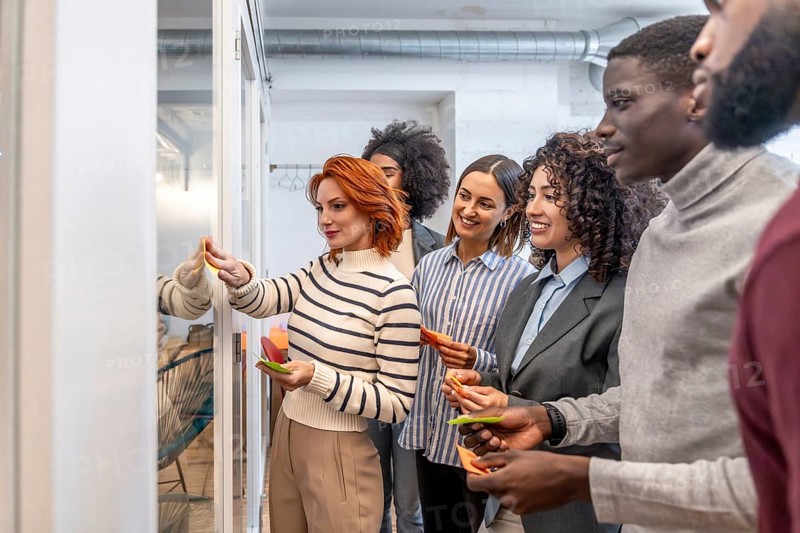 Diverse coworkers using sticky notes on a glass board during brainstorming of a new project