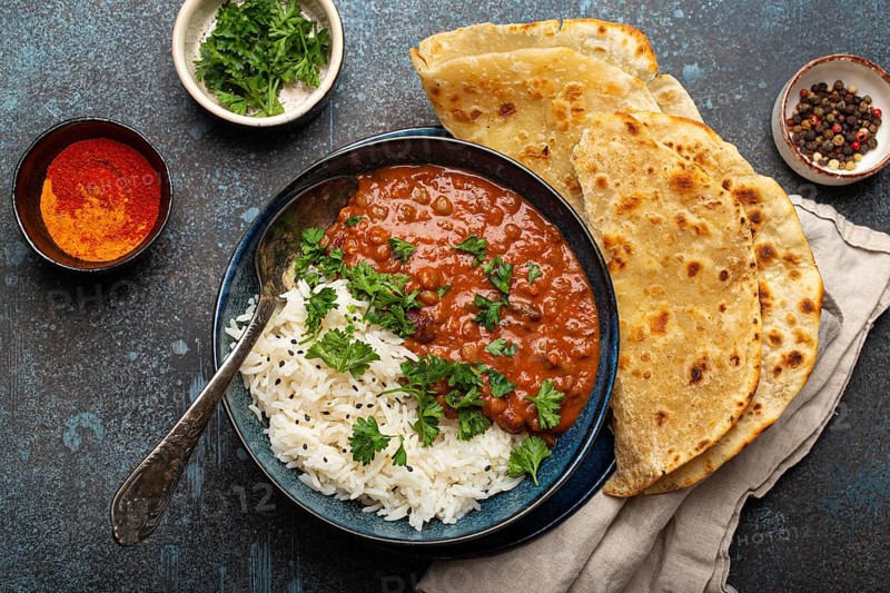 Traditional Indian Punjabi dish Dal makhani with lentils and beans in black bowl served with basmati rice, naan flat bread, fresh cilantro and spoon on blue concrete rustic table top view, food photography, food photography