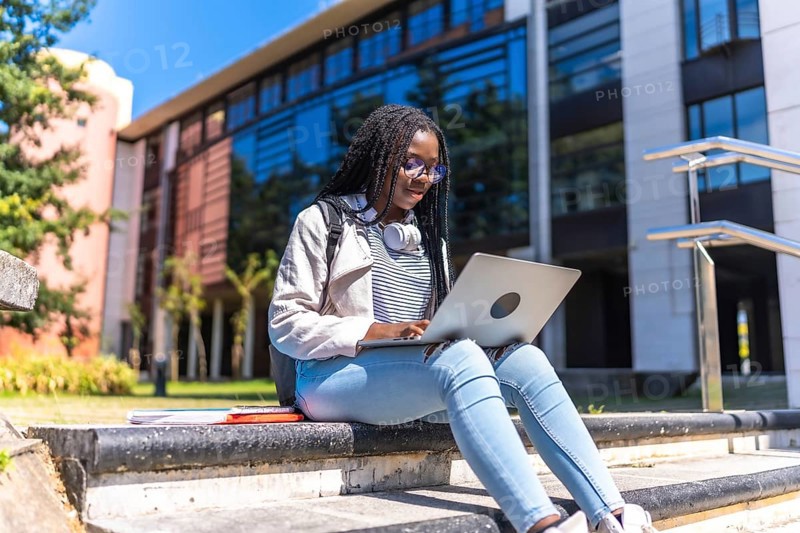 Focused female african university student using laptop sitting on outdoors staircases in the campus