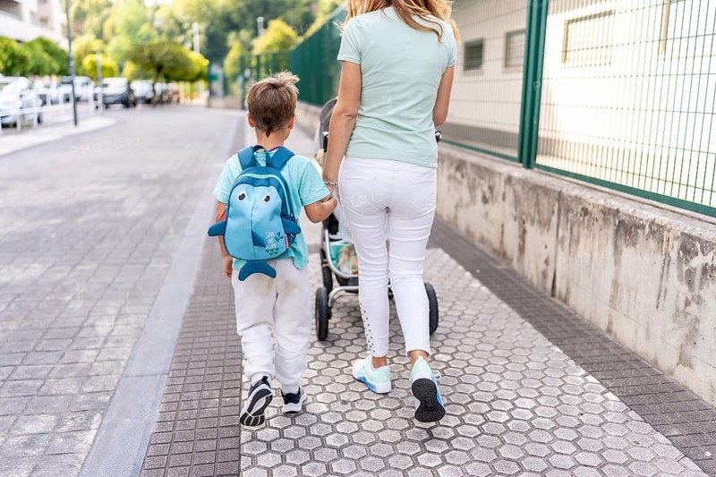 Rear view of a mother and son carrying baby carriage walking to the school together