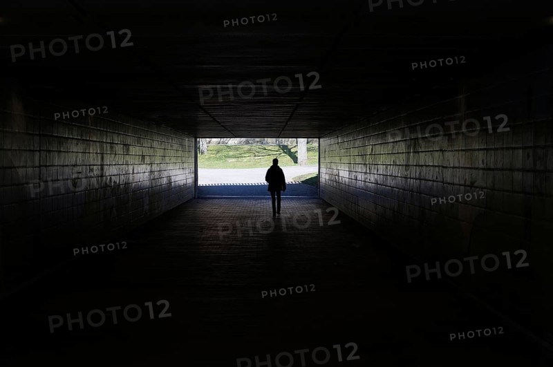 silhouette of a person walking through a dark underpass symbolizing light at the end of the tunnel