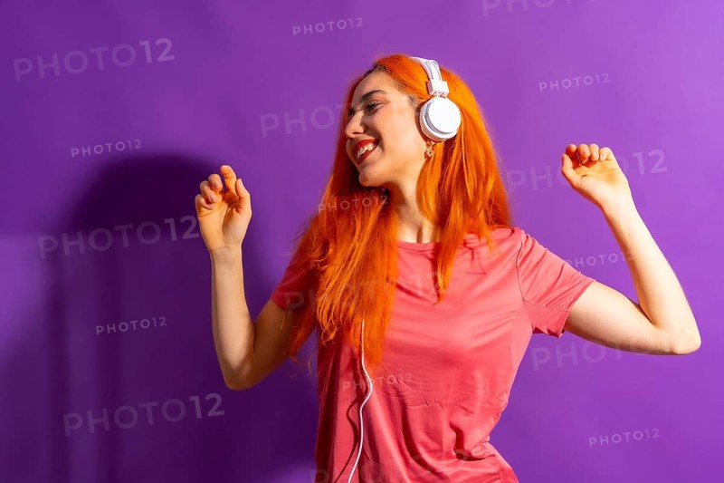 Redhead woman in studio photography dancing on a purple background, with a hard light