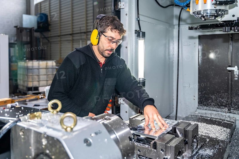 Manual worker with protective goggles and headphones using a milling cnc modern machine