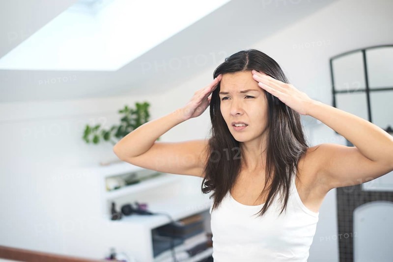Attractive young woman with a migraine headache standing holding her fingers to her temples with her eyes half closed in pain