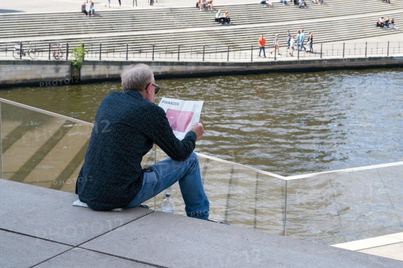 A man sits on a step in the government district of Berlin and reads the financial section of a newspaper