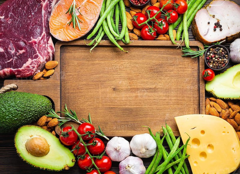 Wooden cutting board and ketogenic low carbs ingredients for healthy weight loss diet, top view, copy space. Keto foods: meat, fish, avocado, cheese, vegetables, nuts. Clean eating, healthy fats