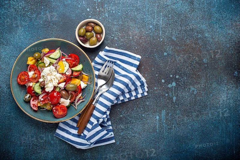 Greek fresh healthy colorful salad with feta cheese, vegetables, olives in blue ceramic bowl on rustic concrete background top view, Mediterranean diet, traditional cuisine of Greece. Space for text, food photography, food photography