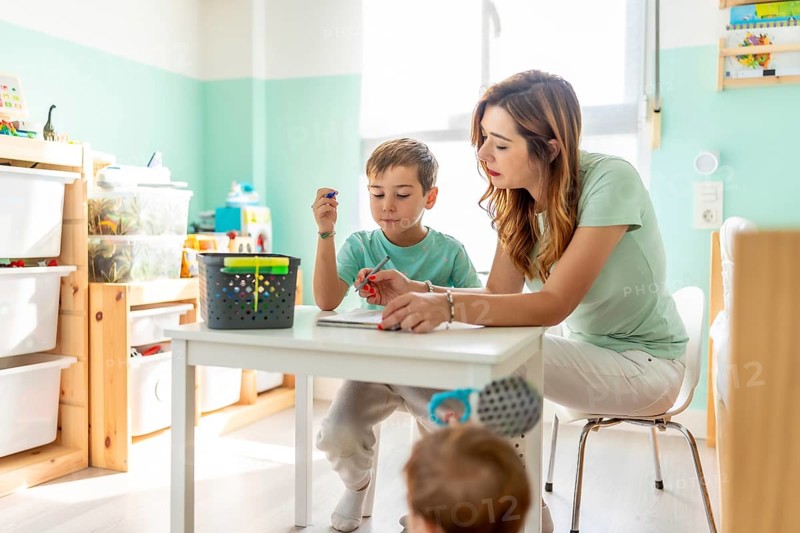 Mother and school boy draw color pencil in the bedroom next to a baby boy