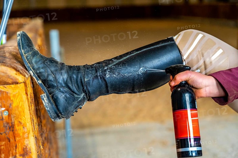 Cropped photo of the hand of a woman cleaning horse riding boots with spray