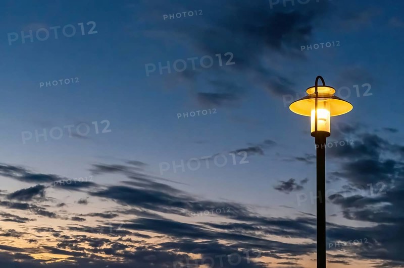 Illuminated street lamp in front of a rainy autumn sky