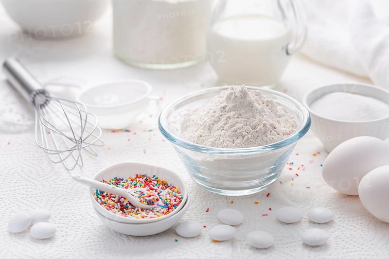 Baking background with flour, eggs, sugar sprinkles, kitchen tools, utensils in white