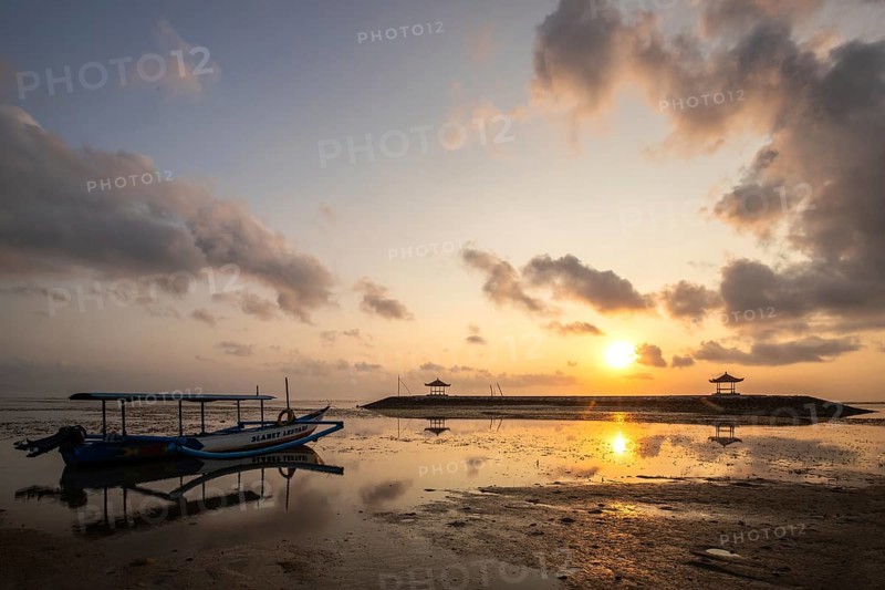 Morning landscape taken on the sandy beach. View over the sea to the horizon with small temples in the water and a jukung, a traditional fishing boat, on the beach. Sunrise in Sanur, Bali, Indonesia, Asia