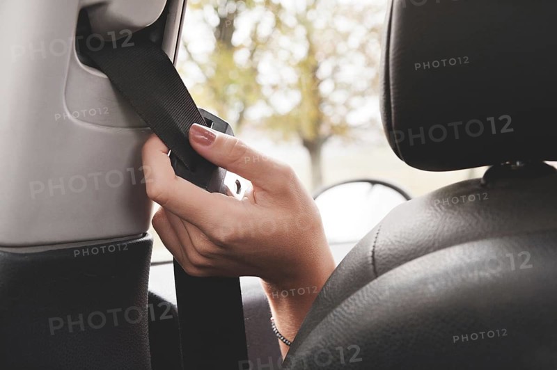 A woman's hand reaches behind her seat belt to fasten it. The concept of safe driving of women by car