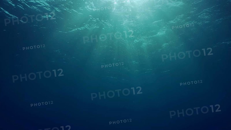 View of sun light from blue abyss, slow motion. Light filters down through blue water. Underwater sun rays in depth ocean. Underwater sun light shine under deep water with ripples on waves surface