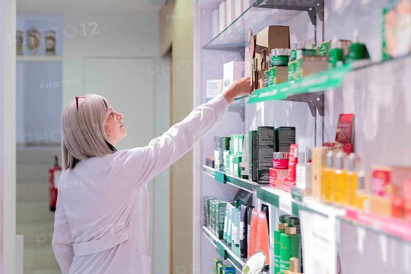 A health professional reviews and organizes a variety of products on the shelves, ensuring quality and accessibility for customers seeking healthcare options