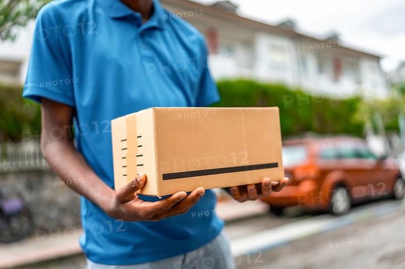 Close-up of a cardboard package on hands of a delivery man on blue uniform standing on street