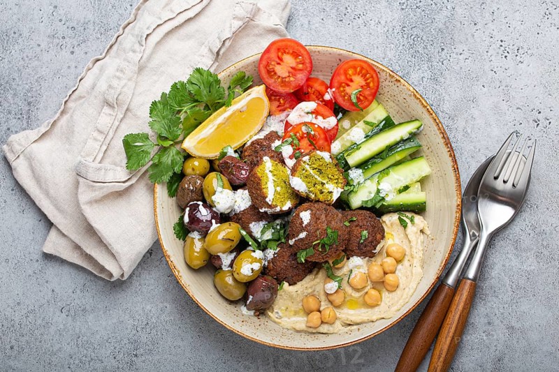 Falafel salad bowl with hummus, vegetables, olives, herbs and yogurt sauce. Vegan lunch plate top view on rustic stone background, healthy meal with falafel and veggies, food photography, food photography