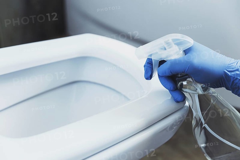 Close up on woman hand gloved in blue rubber protective gloves. Housewife cleaning toilet bowl, seat with detergent liquid in bathroom or restroom. Disinfection, hygiene, cleaning service concept