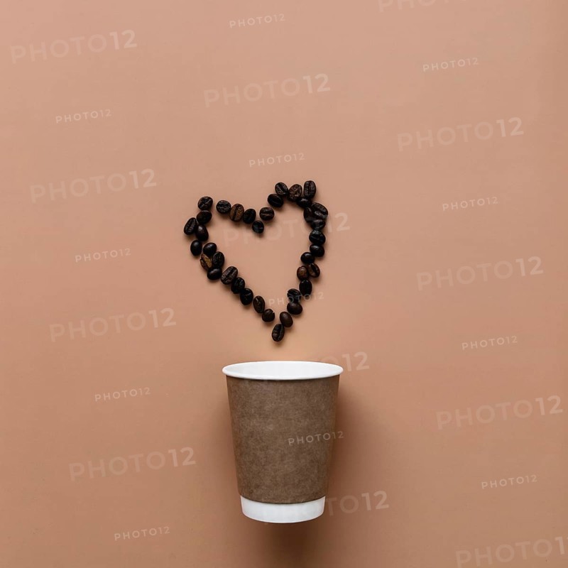 Beige background with paper coffee cup, coffee beans heart shape.