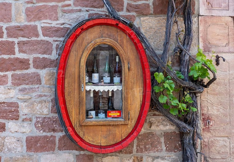 Wine bottles from the Alte Kelter winery in a wine barrel with a glass window on a house wall with a grapevine, Landau-Mörzheim, Rhineland-Palatinate, Germany, Europe