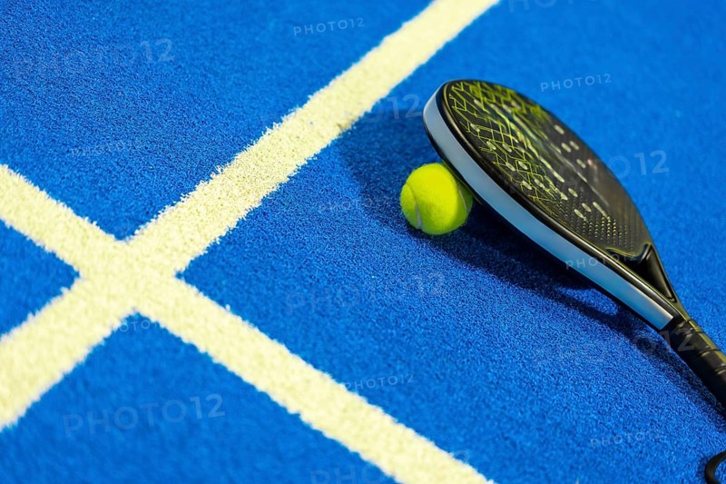 Photo with no people and copy space of a paddle tennis racket leaning on ball in a blue court