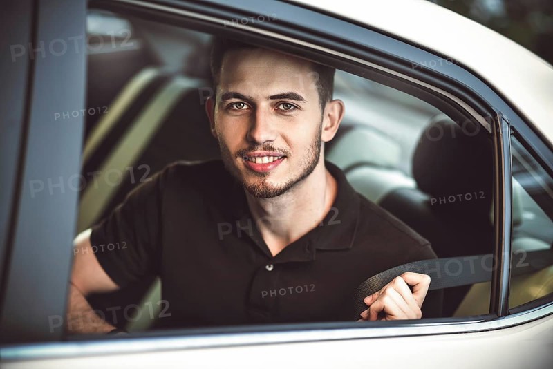 Young, handsome man fastens a seat belt, sitting in the back seat of the car