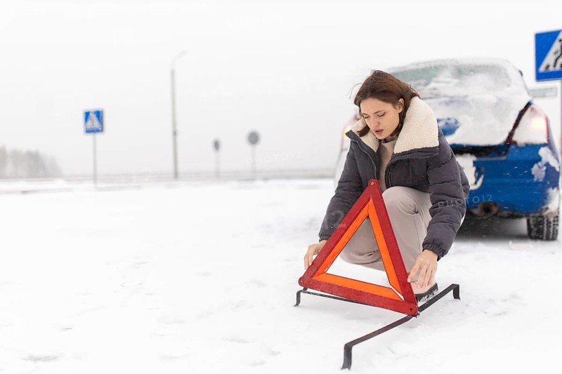 Woman puts up a warning triangle on a snowy road in winter, car breakdown in winter