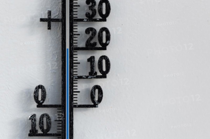 Classic black analog thermometer hanging on white wall displaying blue temperature scale of twenty, 20 degrees celsius