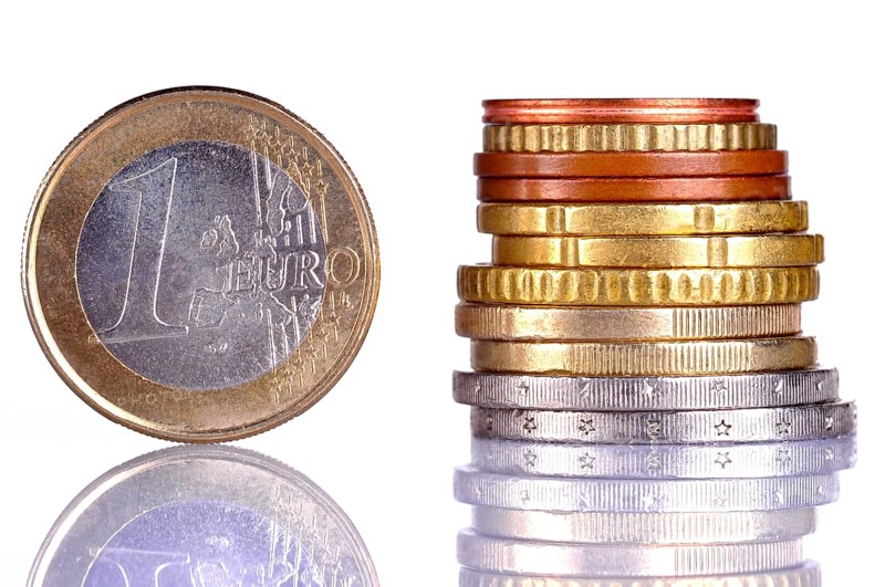 Close up of the oen Euro coin, next to a pile of coins