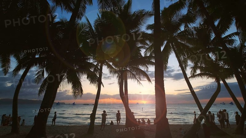 Silhouetted people and palms near sea. Sunset at tropical White beach, Boracay island, Philippines, Asia